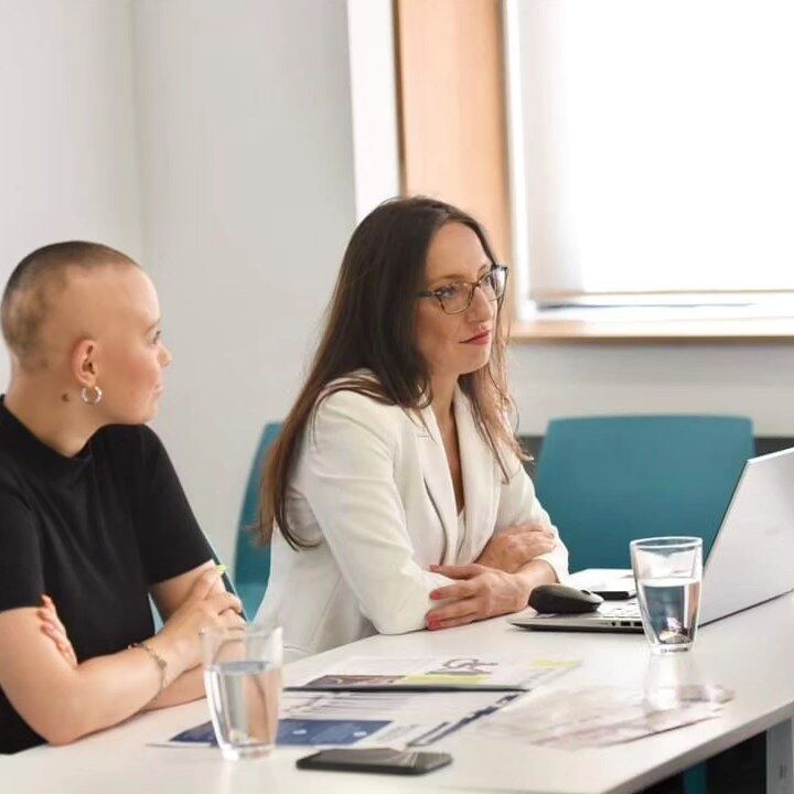 In this picture, you have Elizabeta Jovanovska the CEO, who wears a white blazer and a white T-shirt and Cece, an employee of the company. Cece has Alopecia universalis. She wears a black T-shirt.	